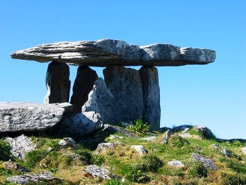 Dolmen de grandes pierres dressées sur une colline herbeuse, sous un ciel bleu