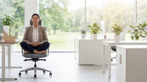 Femme assise en méditation sur une chaise de bureau, dans un espace de travail lumineux ouvert sur la verdure