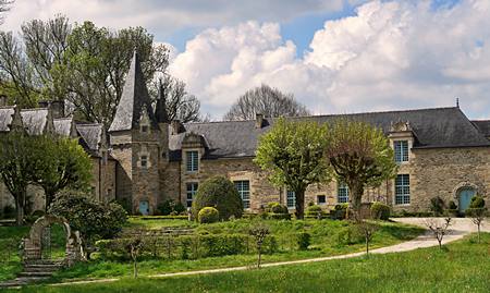 Manoir ancien en pierre, avec sa tourelle et son jardin, sous un ciel de printemps
